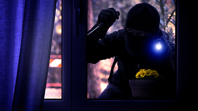 Einrecher leuchtet mit einer Taschenlampe in eine Fenster