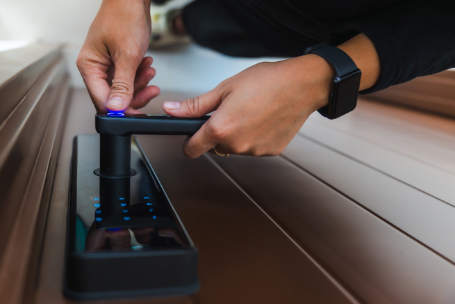 Hände öffnen eine digital gesicherte Türe über einen Fingerabdrucksensor mit Zahlencode