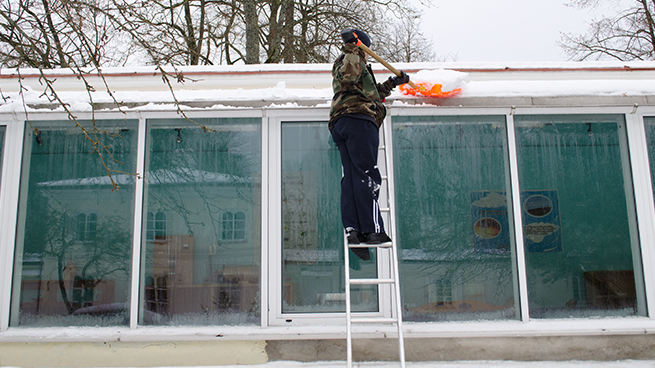 Mann schaufelt Schnee im Winter vom Dach des Wintergartens