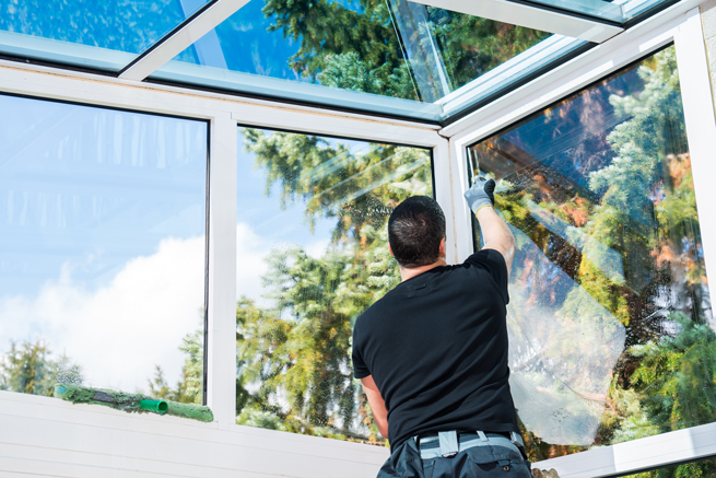 Mann putzt Fensterscheiben im weißen Wintergarten