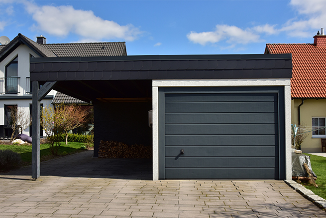 Un grand carport avec un garage intégré sur le côté droit avec une porte de garage à grandes lamelles en anthracite