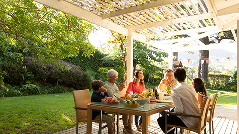 Ein Sommergarten mit weißer Terrassenüberdachung im Sommer mit Menschen, die am Tisch auf der überdachten Terrasse sitzen