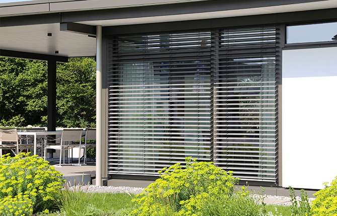 Große Fensterfront mit anthrazitfarbenem Raffstore und Grünfläche