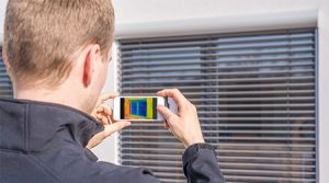 Homme mesurant le passage de la chaleur avec un appareil de mesure devant une fenêtre
