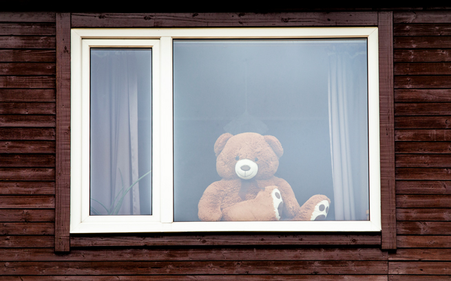 Holz Hausfassade mit Festverglasung hinter der ein Teddybär sitzt und lächelt