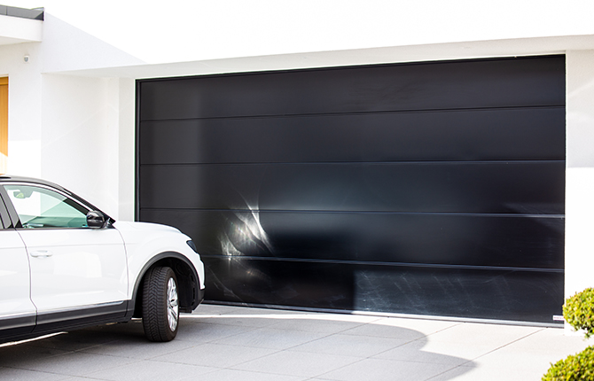 Voiture blanche devant une porte de garage fermée de couleur anthracite