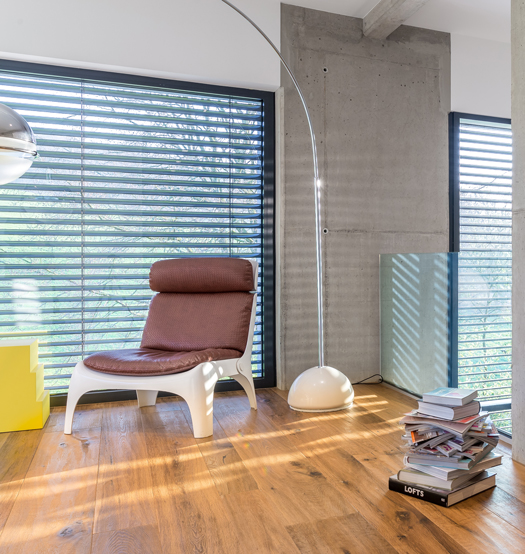 Wohnzimmer mit Lampe und Sessel mit Blick auf zwei Raffstores die herunter gefahren sind