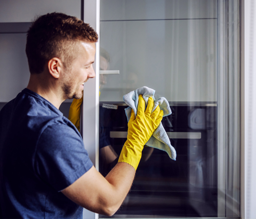Mann putzt Fenster mit gelben Gummihandschuhen und blauem Lappen