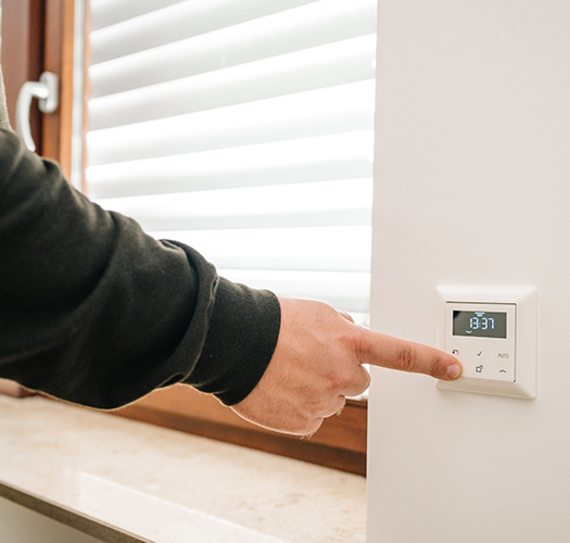 Hand die auf einen Smarthome Schalter zeigt um den Rollladen zu öffnen