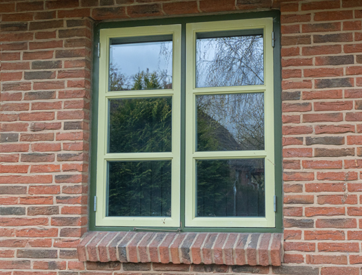 Grünes Fenster mit glasteilenden Sprossen in einer Backsteinwand